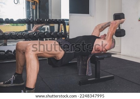 A rugged and old German man does dumbbell pullovers while lying perpendicular to the bench. Training upper body at the gym. Royalty-Free Stock Photo #2248347995