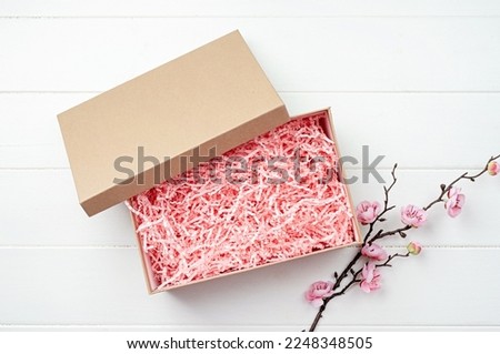 Shredded pink paper packing material in craft gift box with sakura branch. Pink spaghetti shredded packing paper used to protect fragile object while in transport. Mockup design for valentine gift box