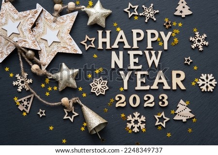 Happy New Year-wooden letters and the numbers 2023 on festive black background with sequins, stars, lights of garlands. Greetings, postcard. Calendar, cover