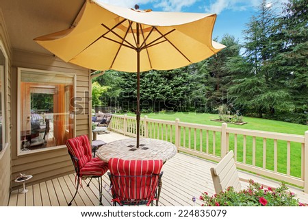 Wooden walkout deck with patio table, umbrella and chairs overlooking backyard landscape