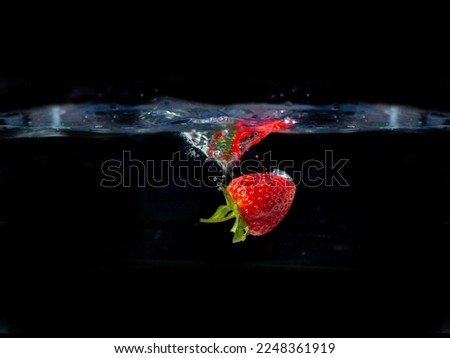 Half Red strawberry fruit falling in water splash on black background.