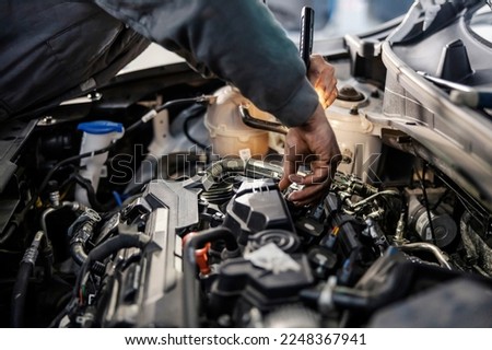 Cropped picture of a mechanic doing car checkup under the hood with flashlight at garage.