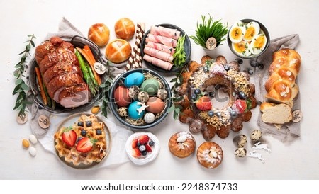 Traditional Easter dinner or  brunch with ham, colored eggs, hot cross buns, cake and vegetables. Easter meal dishes with holday decorations. Top view, flat lay Royalty-Free Stock Photo #2248374733