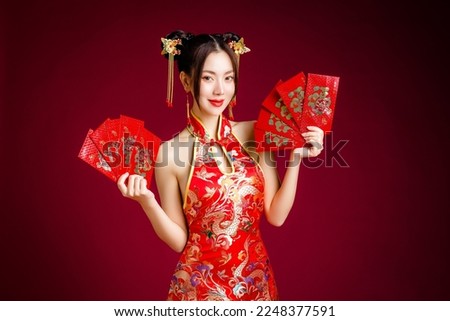 Beautiful Asian woman with clean fresh skin wearing traditional cheongsam dress holding red envelopes or Ang Pao on red background. Happy Chinese new year. Chinese text means great luck great profit. Royalty-Free Stock Photo #2248377591
