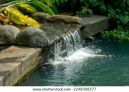 Water flows from the rocks in the residential garden Royalty-Free Stock Photo #2248388377