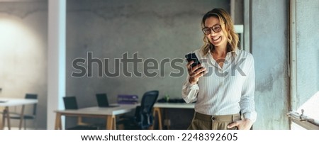 Smiling businesswoman using her phone in the office. Small business entrepreneur looking at her mobile phone and smiling while communicating with her office colleagues Royalty-Free Stock Photo #2248392605