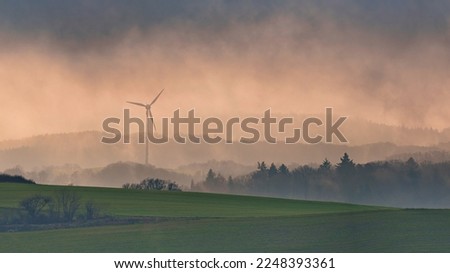 Foggy nature landscape with mountains and wind turbines at village. Royalty-Free Stock Photo #2248393361