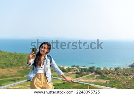 Young Asian woman traveler using mobile phone taking selfie while solo travel on tropical island mountain in summer sunny day. Attractive girl enjoy outdoor lifestyle in holiday beach vacation trip