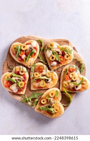 Heart shape mini pizzas on wooden board for Valentines day holiday, top view. Valentines day food in shape of heart