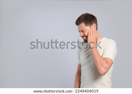 Man suffering from ear pain on grey background Royalty-Free Stock Photo #2248404019