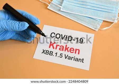 Kraken virus. Doctor's hand in blue glove writing on white paper the text "Covid-19 Kraken XBB.1.5 Variant" with protection masks on the background. Concept for the new Covid 19 Kraken variant