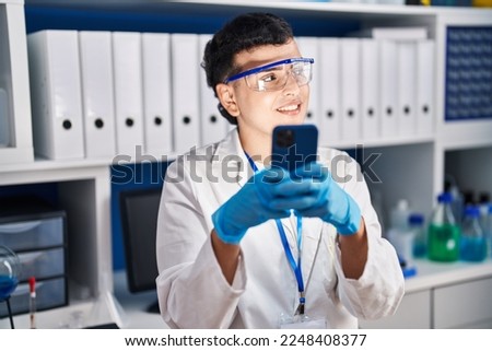 Young non binary man scientist smiling confident using smartphone at laboratory