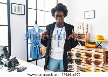African young woman working as manager at retail boutique pointing down looking sad and upset, indicating direction with fingers, unhappy and depressed. 