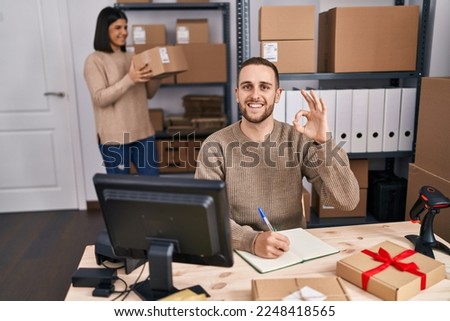 Two young people working at small business ecommerce doing ok sign with fingers, smiling friendly gesturing excellent symbol 