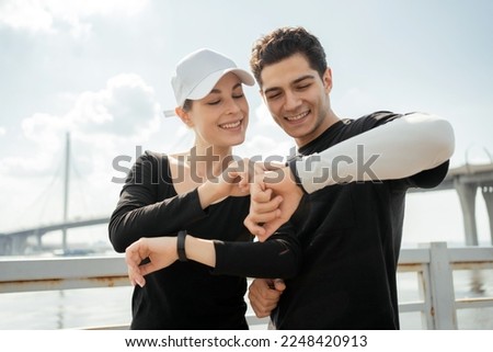 Using a fitness watch, a smart bracelet with cardio and pulse oximeter. A sporty female athlete and a man in a sports uniform. Young couple workout exercise running outdoors Royalty-Free Stock Photo #2248420913