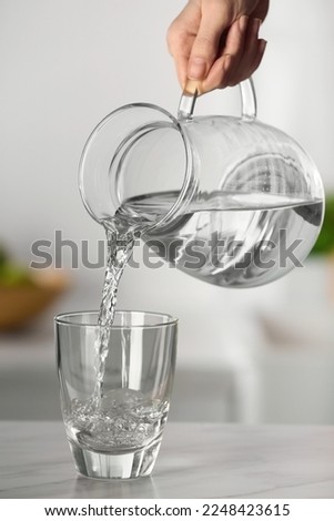 Woman pouring water from jug into glass on white marble table in kitchen, closeup Royalty-Free Stock Photo #2248423615