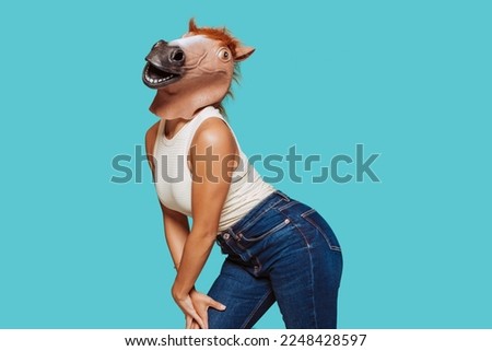 Portrait of a funny girl in a horse head mask posing at studio, isolated over blue background.  Royalty-Free Stock Photo #2248428597