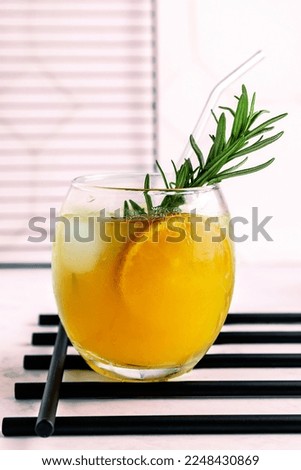 Fresh organic citrus juice in glass. Cold natural summer drink with citrus slices, ice and rosemary branch on blurred background. Close up. Selective focus.