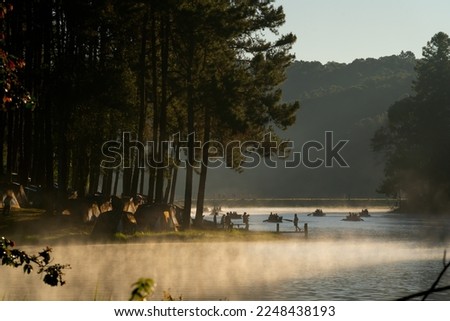 Silhouette of many travelers enjoy to take photo at waterfront in national park with beautiful environment of mist and warm light in early morning with serveral activities.
