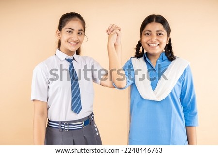 Happy Rural and Modern Indian student schoolgirls wearing school uniform standing together join hands isolated over beige background, Closeup, Studio shot, Education concept.