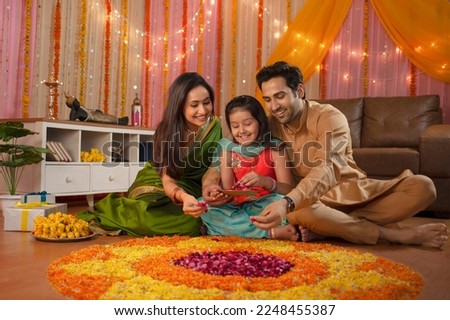 Young Indian family making flower rangoli for Diwali festival celebration. A healthy family sitting together and decorating the house, making flower rangoli, daughter holding flower tray - In... Royalty-Free Stock Photo #2248455387