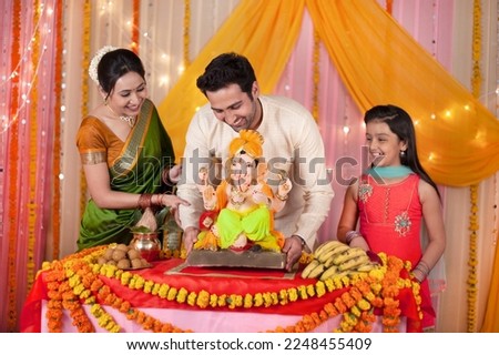 Cheerful Indian family welcoming Lord Ganesha idol on Ganesh ,Ganesh Chaturthi. Smiling and happy family welcoming Lord Ganesh idol for Ganesh Chaturthi - Table decorated with marigold fl... Royalty-Free Stock Photo #2248455409