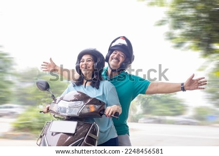 Happy senior indian couple wearing helmet riding motor scooter on road. Retirement life, Adventure and travel, Closeup Royalty-Free Stock Photo #2248456581