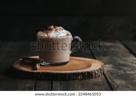 A closeup shot of a glass of hot chocolate on a wooden board, with cream on top