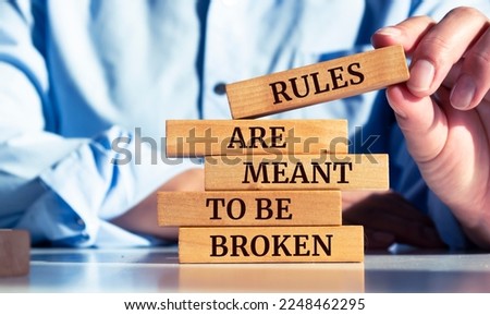 Closeup on businessman holding a wooden block with "RULES ARE MEANT TO BE BROKEN" message