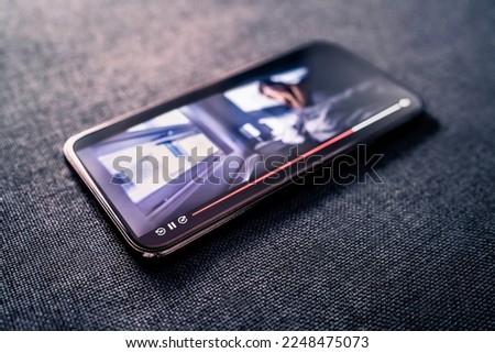 Movie stream or video player in mobile phone. Watching series online with smartphone concept. Film on demand service. Mockup VOD in screen. Scary horror or thriller tv show. Cellphone on couch. Royalty-Free Stock Photo #2248475073
