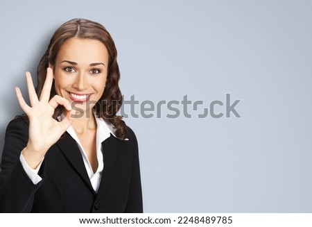 Portrait image of happy smiling business woman in black confident suit showing ok okay gesture, isolated over grey background. Female executive office worker, teacher or real estate agent.
