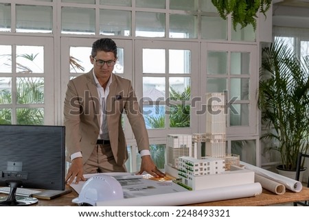 Young attractive male CEO or architecture expresses his face and body posture to celebrate success from his project. Young designer works with his plan and model in an office