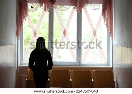 The girl stands at the school windows glued crosswise. War in Ukraine. High resolution photo. Selective focus.