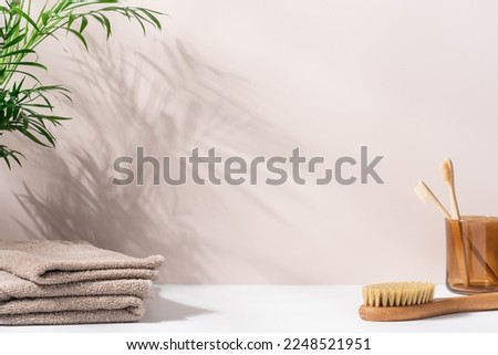 Сlean bathroom background with green palm branch that casts shadows, terry cotton towels and bamboo brushes. Mockup space for presentation of beauty products