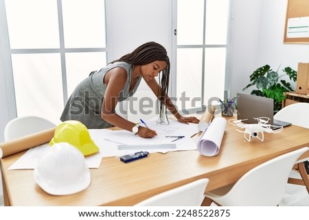 Young african american woman architect writing on house plans at architecture studio Royalty-Free Stock Photo #2248522875