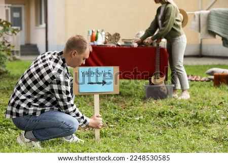 Man with sign Yard sale and woman near table of different items outdoors