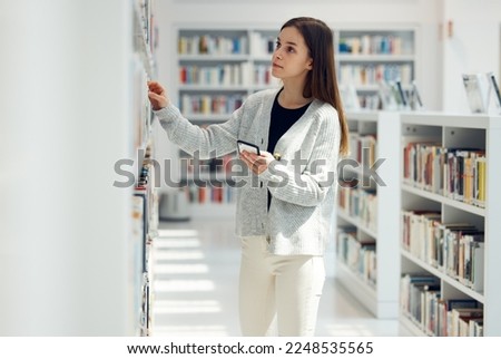 Library, book choice and student with phone in university, college or school. Learning, education scholarship or woman holding mobile looking for books by bookshelf for reading, knowledge or studying