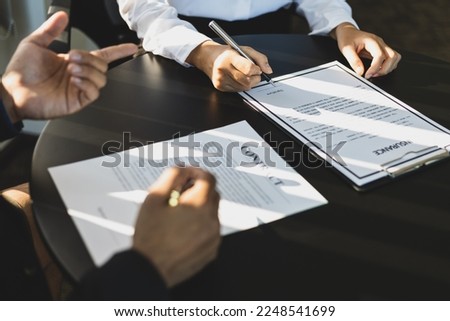 Businessman in suit in his office showing an insurance policy and pointing with a pen where the policyholder must to sign. Insurance agent presentation and consulting insurance detail to customer.