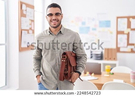 Young hispanic man business worker smiling confident holding briefcase at office Royalty-Free Stock Photo #2248542723