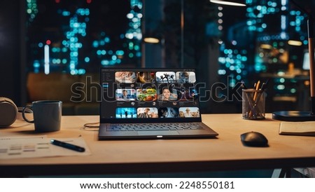 Laptop Standing on a Desk with a Video Streaming Platform Displayed on Screen. Table with Computer, Coffee Mug, Headphones and Notebook in Creative Office at Night. Royalty-Free Stock Photo #2248550181