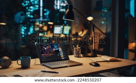 Laptop Standing on a Desk with a Video Streaming Platform Displayed on Screen. Table with Computer, Coffee Mug, Headphones and Notebook in Creative Office at Night. Royalty-Free Stock Photo #2248550207