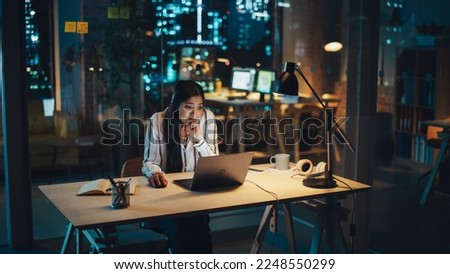 Creative Multiethnic Female Working on Laptop Computer in a Company Office at Night. Surprised Project Manager Receiving an Email, Browsing Internet, Working On a Corporate Strategy.