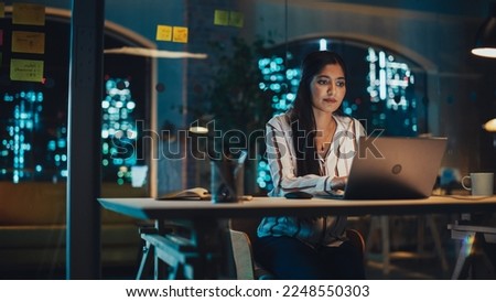 Beautiful Female in a Striped White Shirt Sitting at a Desk in Creative Office, Working on Tasks on Laptop Computer. Young Creative Specialist Writing Corporate Project Plan for Marketing Agenda.