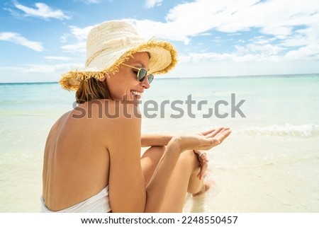 Portrait of smiling woman on sandy tropical beach wearing white bikini and summer hat. Face of beautiful young girl enjoying seaside. Copy space. Island vibes. 
