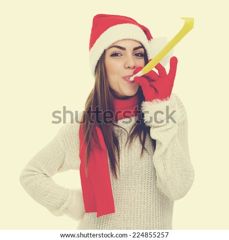 Closeup studio shot of beautiful Christmas girl. Santa woman with hat, scarf and gloves blowing a party whistle celebrating New Year. Square format image. Instant looking filter applied