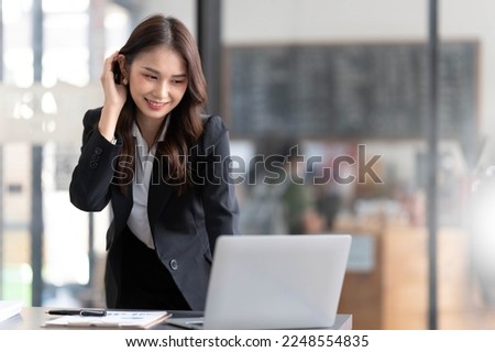 Focused young businesswoman standing at table in office, using laptop, looking at computer screen, reading or writing business email, searching information in internet, working on project