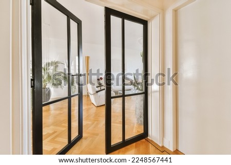 the inside of a house with wood flooring and black double doors leading to an open living room on one side Royalty-Free Stock Photo #2248567441