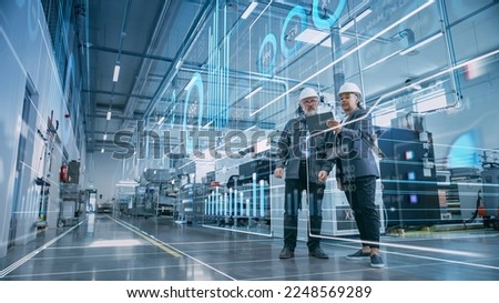 Factory Digitalization: Two Industrial Engineers Use Tablet Computer, Visualize the Wall of Big Data Statistics, Optimization of High-Tech Electronics Facility. Industry 4.0 Machinery Production Royalty-Free Stock Photo #2248569289