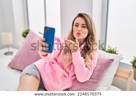 Young woman making selfie by smartphone sitting on bed at bedroom