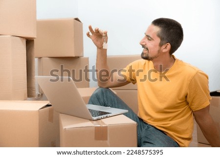 Happy caucasian man with the keys of his new home flat apartment house and laptop between boxes. High quality photo